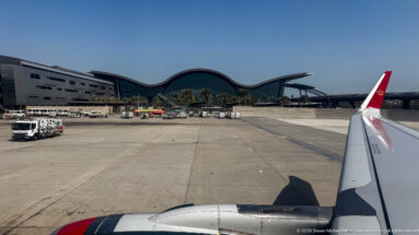 Aircraft wing beside the apron with Queen Alia International Airport’s glass terminal and wave-like roof beyond.