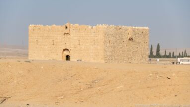 Small rectangular stone fort with arched doorway, narrow openings, and crenellated parapets in a dry landscape.
