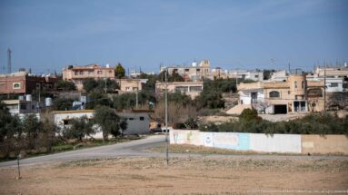 Scattered pale houses and olive trees on gently rising terrain along the outskirts of Amman.