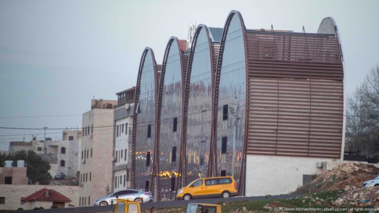 Modern Amman building with repeated curved roof forms, reflective glass, horizontal slats, and vehicles along the street.
