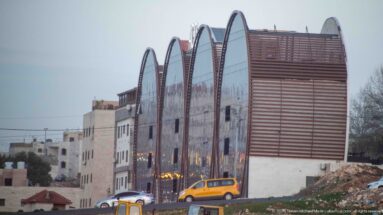 Modern Amman building with repeated curved roof forms, reflective glass, horizontal slats, and vehicles along the street.