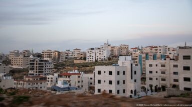 White and pale-stone apartment buildings spread across an Amman hillside above exposed rock and a rough open foreground.