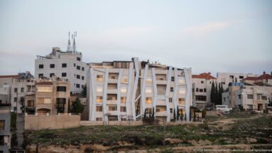 White Amman apartment building with angular projecting frames and diagonal façade elements among pale residential blocks.