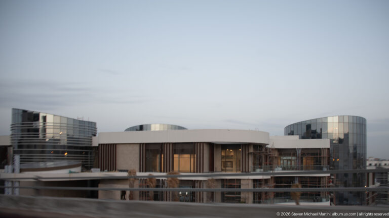 Modern Amman complex with rounded low buildings, cylindrical glass towers, and rectilinear volumes seen at dusk.