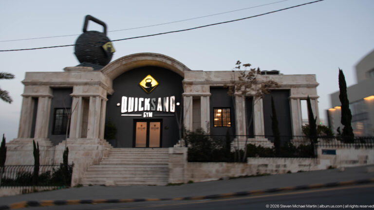 Quick Sand Gym in Amman, with a large illuminated sign on a symmetrical pale stone façade with columns and an arch.