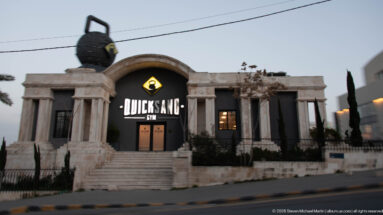 Quick Sand Gym in Amman, with a large illuminated sign on a symmetrical pale stone façade with columns and an arch.