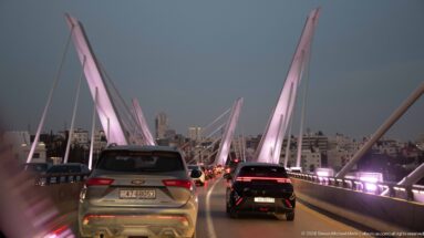 Cars moving across the Wadi Abdoun Bridge beneath pink-lit pylons and diagonal cables, with Amman ahead.