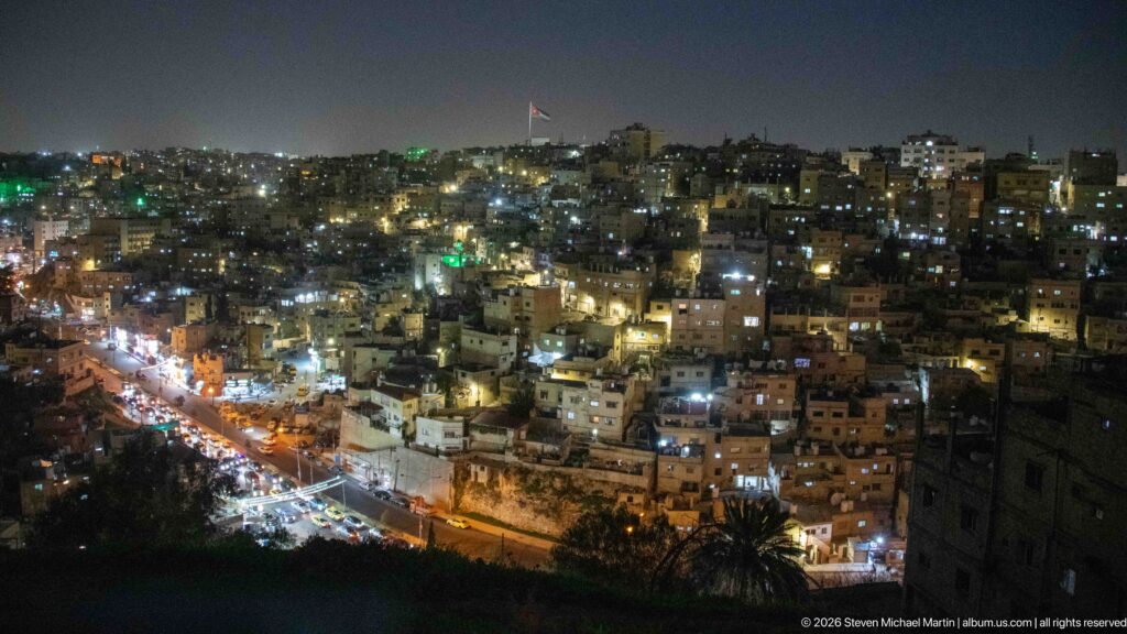 Wide night panorama of Amman with dense hillside housing and a brightly lit road along the lower slope.
