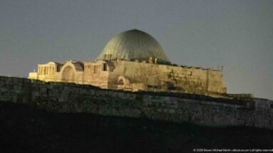 Historic stone building on a hill at dusk with a large ribbed dome and arched masonry forms.