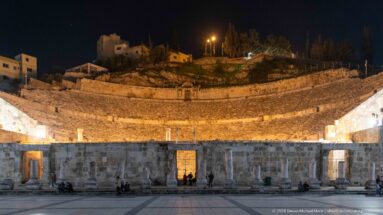 Amman Roman Theater at night, showing the illuminated semicircular seating above the stage building and plaza.