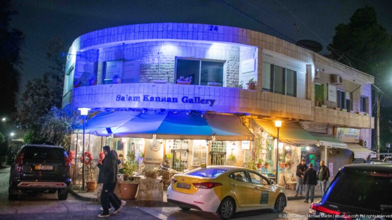 Salem Kanaan Gallery illuminated at night on an Amman street with pedestrians, cars, and shop displays.