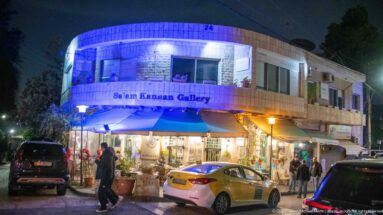 Salem Kanaan Gallery illuminated at night on an Amman street with pedestrians, cars, and shop displays.