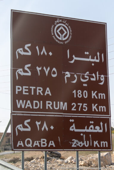 Brown bilingual road sign listing Petra 180 km, Wadi Rum 275 km, and Aqaba about 280 km.