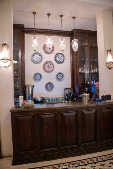 Dark wooden restaurant counter beneath hanging lights, with colorful ceramic plates arranged on the wall.