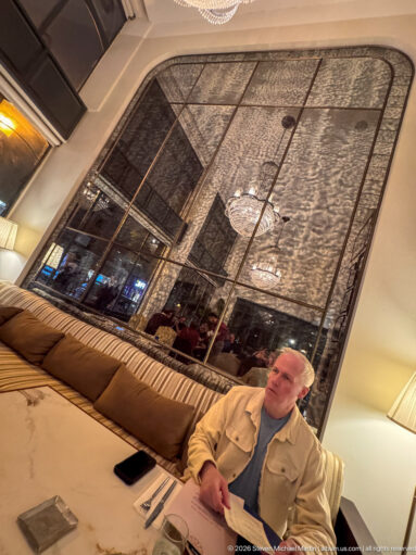 Diner seated on a banquette beside a tall decorative mirror in an elegant restaurant interior.