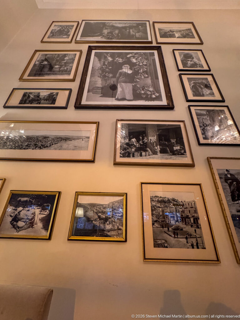 Wall densely arranged with framed black-and-white portraits and historic scenes above an interior space.