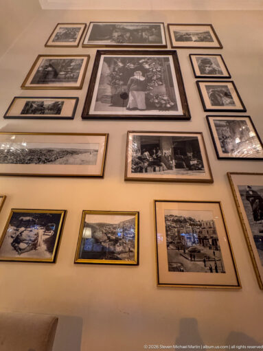 Wall densely arranged with framed black-and-white portraits and historic scenes above an interior space.