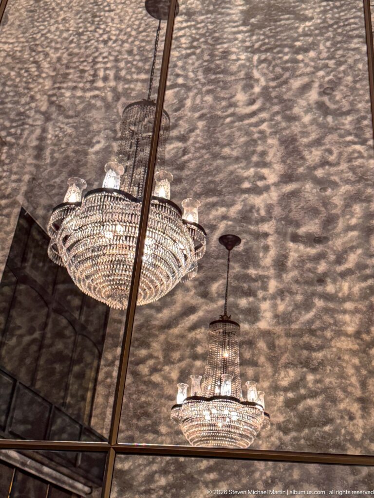Two crystal chandeliers hanging beneath a mirrored ceiling filled with warm patterned reflections.