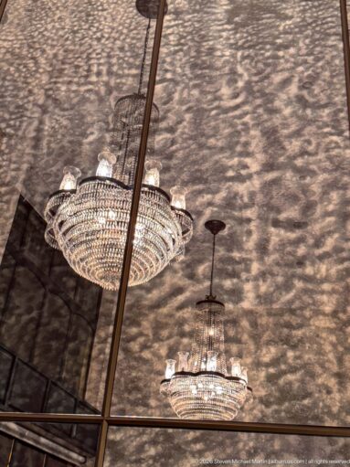 Two crystal chandeliers hanging beneath a mirrored ceiling filled with warm patterned reflections.