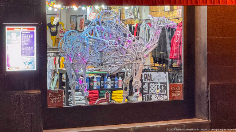 Large openwork wire animal sculpture displayed in a shop window amid colorful merchandise.
