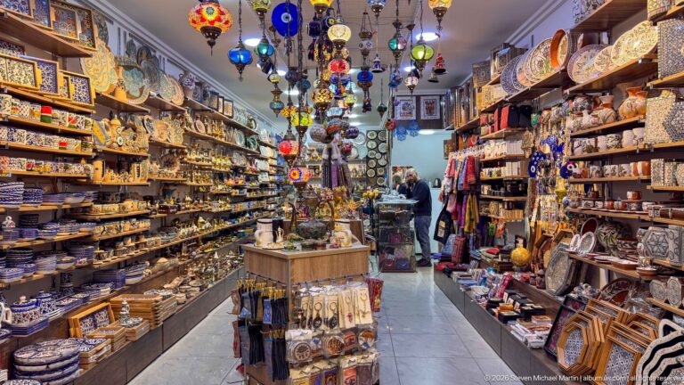 Narrow souvenir shop crowded with ceramics, hanging lamps, textiles, boxes, and colorful decorative goods.