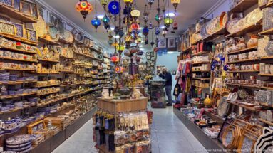 Narrow souvenir shop crowded with ceramics, hanging lamps, textiles, boxes, and colorful decorative goods.