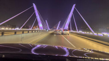 Cars drive beneath purple-lit cable-stayed pylons on a bridge in Amman at night.