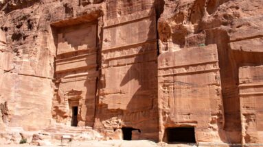 Adjacent monumental tomb façades with recessed panels and small doorways carved into Petra sandstone.
