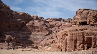 Wide Petra valley view with theater seating at left, tall carved façades at right, and visitors below.