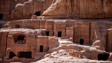 Cluster of dark rectangular chamber entrances cut into smooth, weathered red sandstone at Petra.