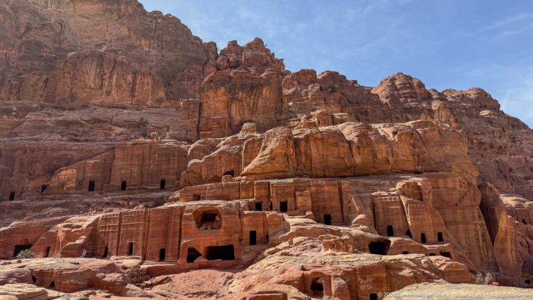 Multiple rows of rectangular rock-cut tomb openings spread across a weathered sandstone cliff at Petra.