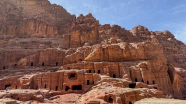 Multiple rows of rectangular rock-cut tomb openings spread across a weathered sandstone cliff at Petra.