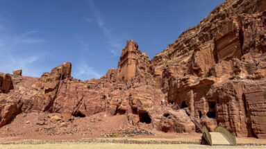 Visitors ascend a steep path among monumental rock-cut tomb façades and chambers in Petra’s sandstone cliffs.