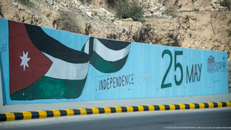 Roadside mural with Jordanian flag, Independence Day wording, and large 25 May date on a turquoise wall.