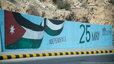 Roadside mural with Jordanian flag, Independence Day wording, and large 25 May date on a turquoise wall.