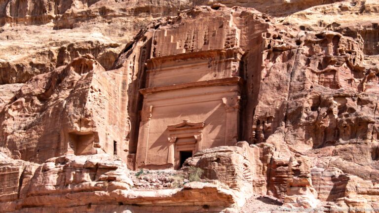 Monumental rectangular rock-cut tomb façade with small doorway carved into Petra’s weathered sandstone cliff.