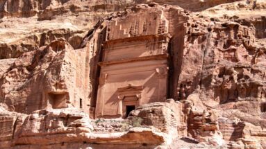 Monumental rectangular rock-cut tomb façade with small doorway carved into Petra’s weathered sandstone cliff.