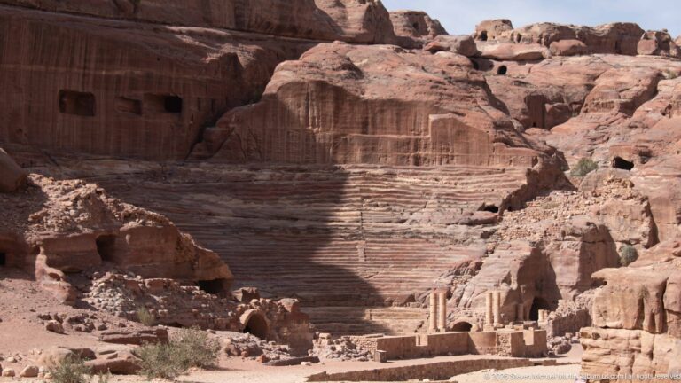 Wide view of Petra’s rock-cut Theater and stage remains set directly against the surrounding sandstone cliffs.