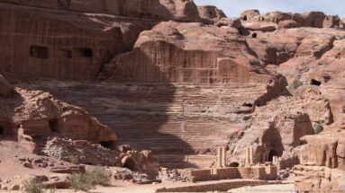 Wide view of Petra’s rock-cut Theater and stage remains set directly against the surrounding sandstone cliffs.