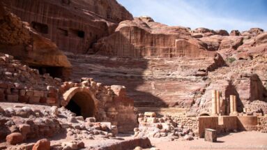 Broad view of Petra’s Theater with rock-cut seating, masonry arch, columns, and surrounding sandstone ruins.
