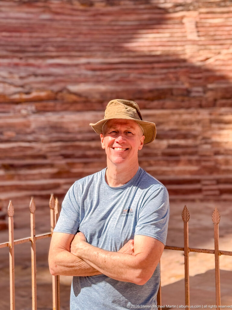 Smiling visitor in a sun hat stands before the blurred sandstone seating tiers of Petra Theater.