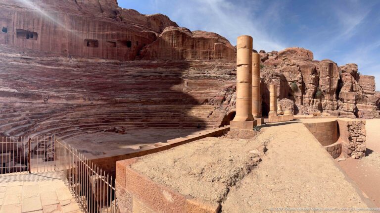 Side view of Petra’s rock-cut Theater with stepped sandstone seating, standing columns, and stage-area remains.