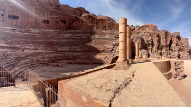 Side view of Petra’s rock-cut Theater with stepped sandstone seating, standing columns, and stage-area remains.