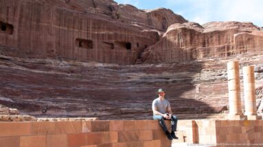 Rock-cut stepped seating and stage area of Petra’s Theater, with a visitor seated among the sandstone remains.