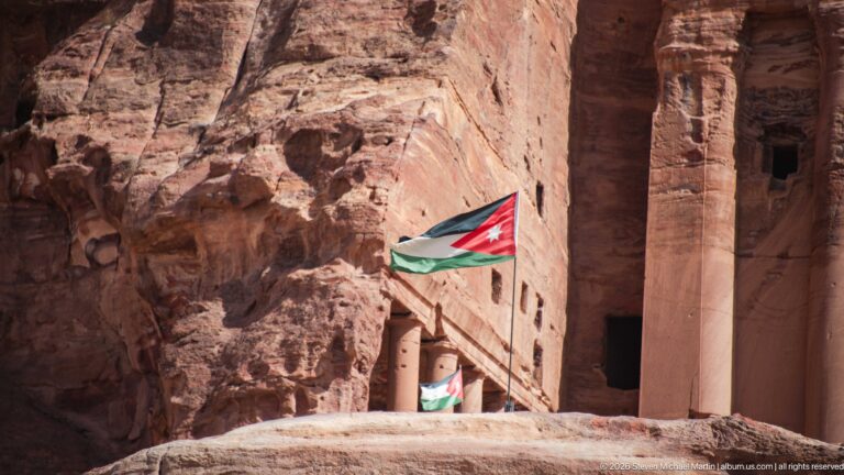 Large Jordanian flag at a monumental rock-cut sandstone entrance within Petra’s Royal Tombs complex.
