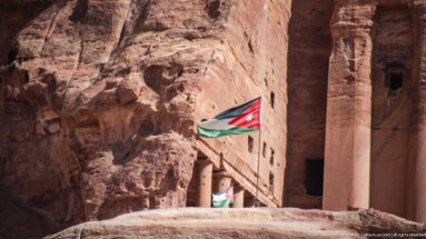 Large Jordanian flag at a monumental rock-cut sandstone entrance within Petra’s Royal Tombs complex.