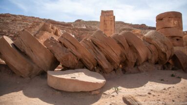 Large fallen cylindrical column drums beside bases and architectural fragments in Petra’s Great Temple complex.