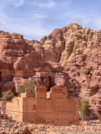 Long sandstone mass of Qasr al-Bint seen from a distance against layered Petra cliffs with rock-cut openings.