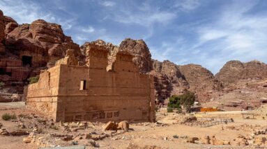 Wide view of Qasr al-Bint Temple amid foundations and stone remains with Petra’s mountains behind.