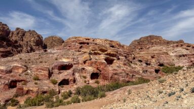 Several small dark rock-cut openings scattered across layered red sandstone hills with sparse shrubs and rubble.